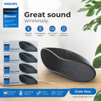 Philips Bluetooth portable speaker shown on a wooden surface with product packaging boxes, promotional text, and feature icons. The speaker is black with a textured grille and control buttons on top.