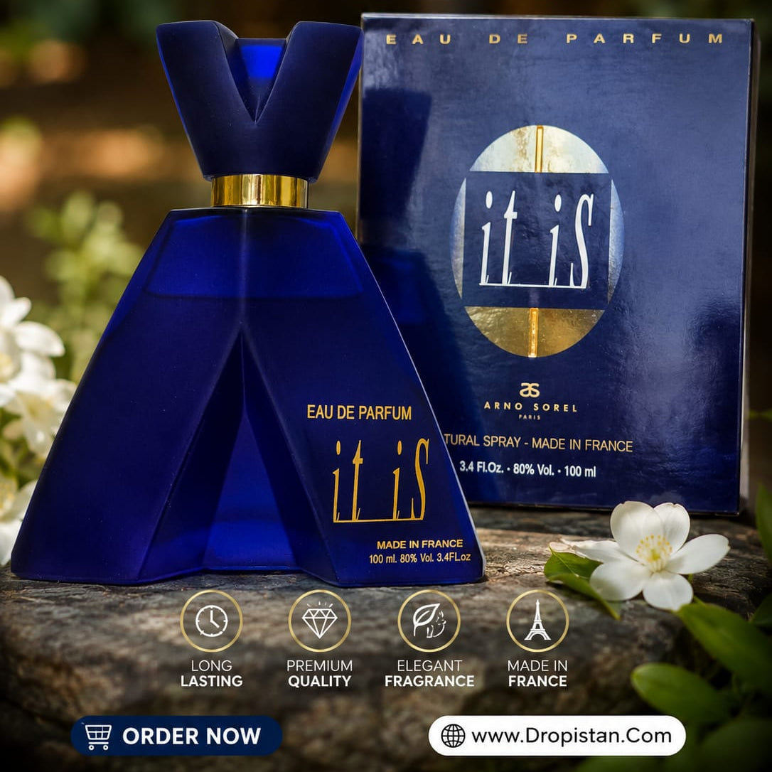 A dark blue perfume bottle and its matching box for 'it is' Eau De Parfum, displayed on a rustic stone surface with white flowers and a blurred green garden background. The image includes promotional text overlays at the top and bottom.