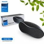 Philips portable Bluetooth speaker in black, shown next to its retail packaging box on a white background with decorative green leaves in the top right corner.